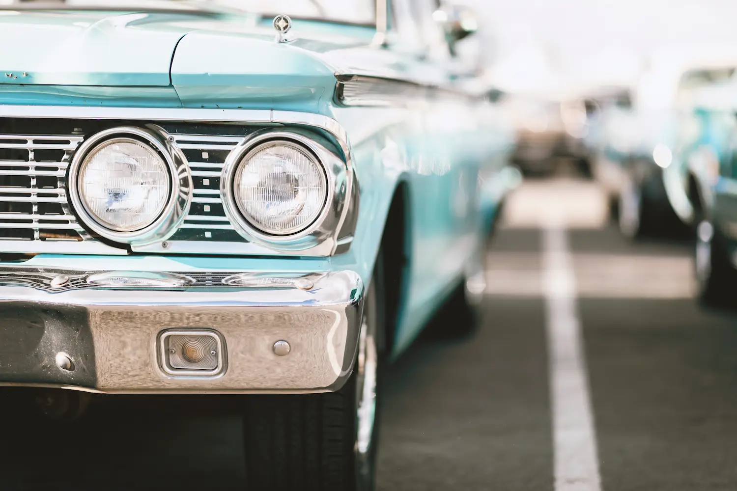 Close-up of a teal vintage classic car parked in a row of antique vehicles at a car show.